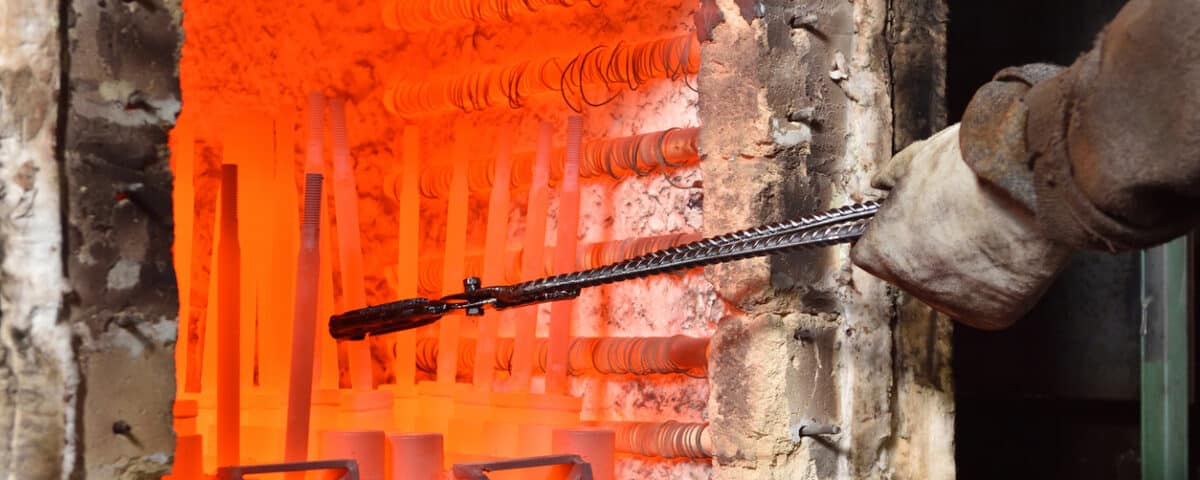 Worker pulls out the heated parts with tongs from an electric furnace for hardening metal. Dangerous work with high temperatures in heavy industry in a valve manufacturing plant