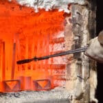 Worker pulls out the heated parts with tongs from an electric furnace for hardening metal. Dangerous work with high temperatures in heavy industry in a valve manufacturing plant