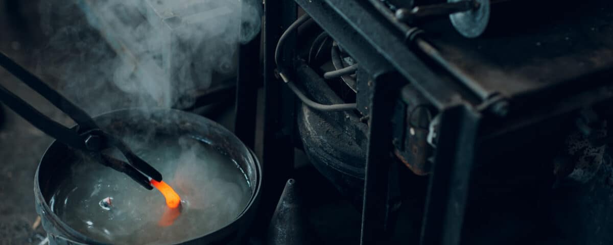 Blacksmith forges and tempering metal horseshoe in jar with water at forge